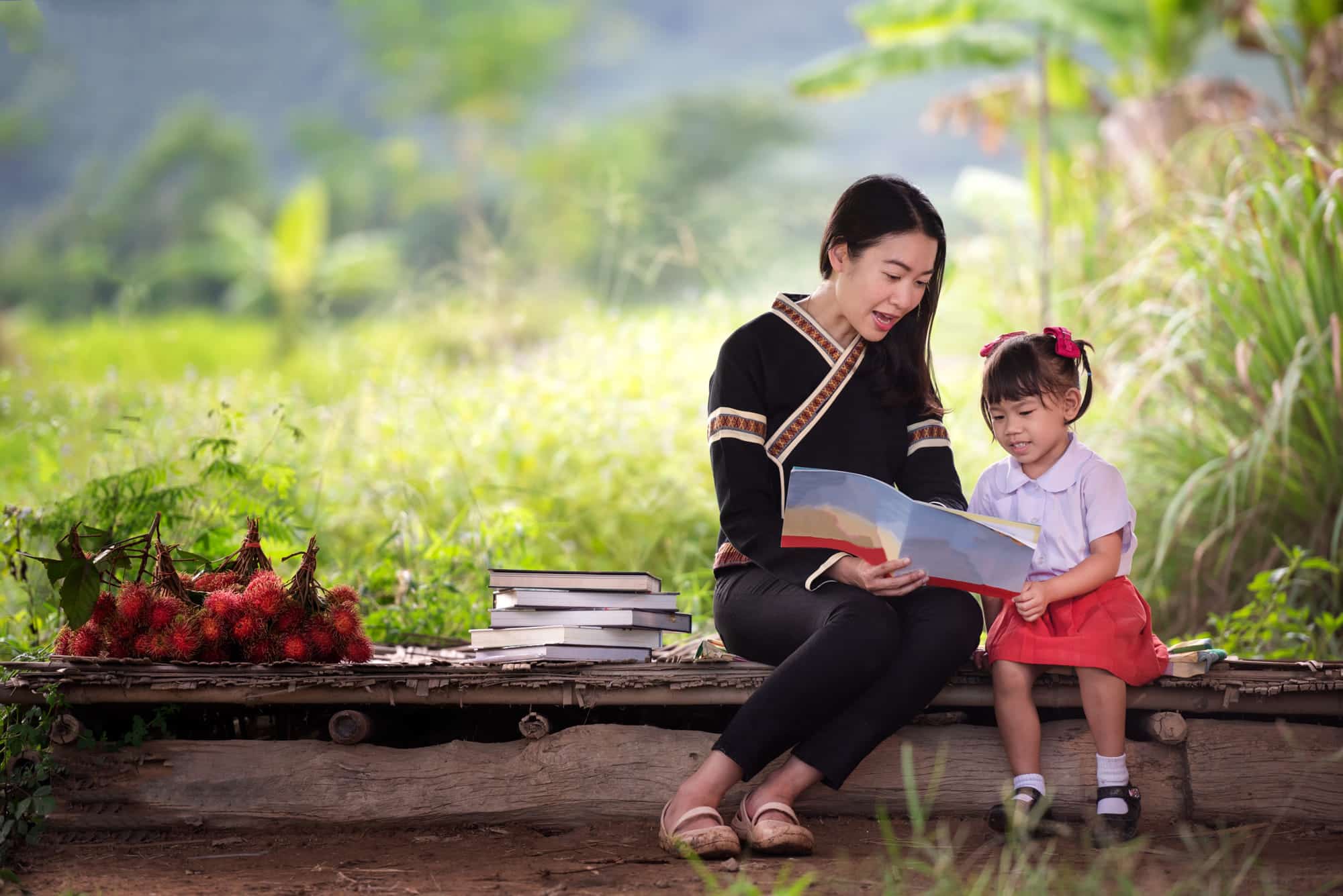 Child reading with mother on a bench outside.