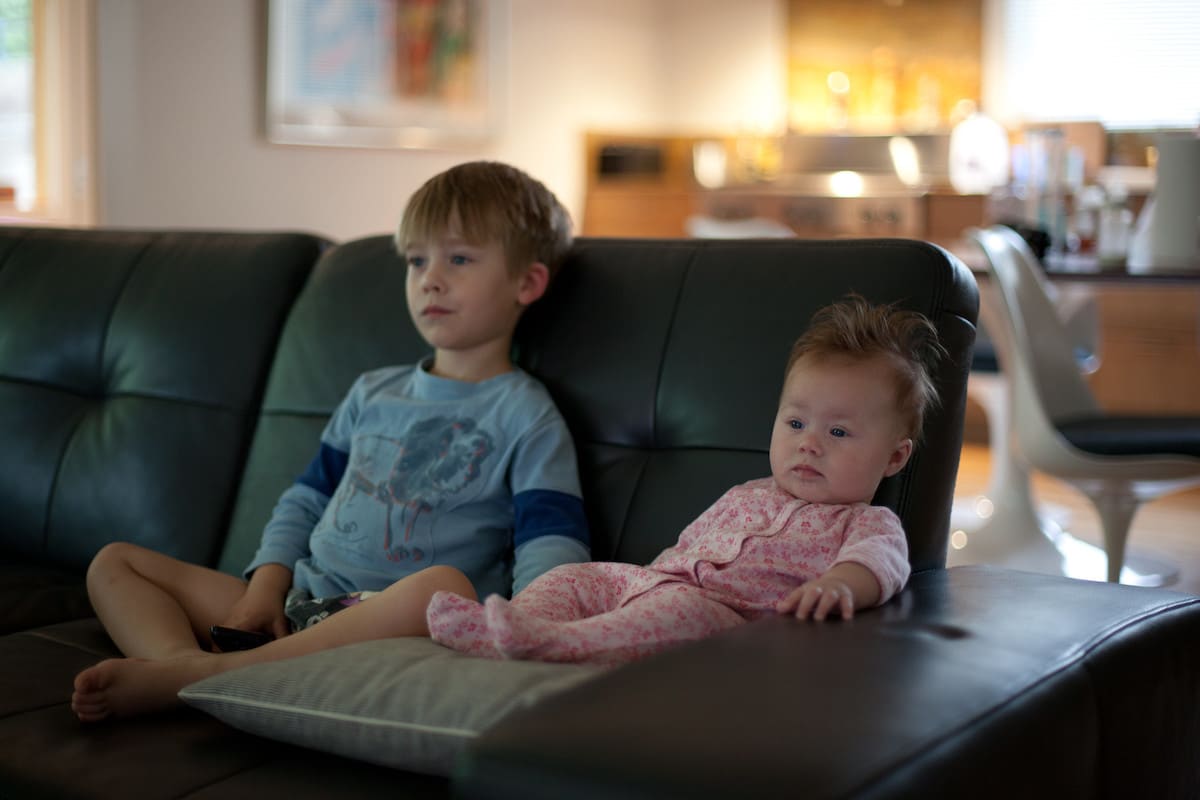 Two children sitting on sofa watching TV.