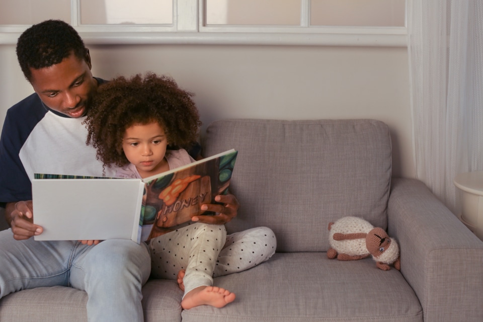 Child reading with father on the sofa.