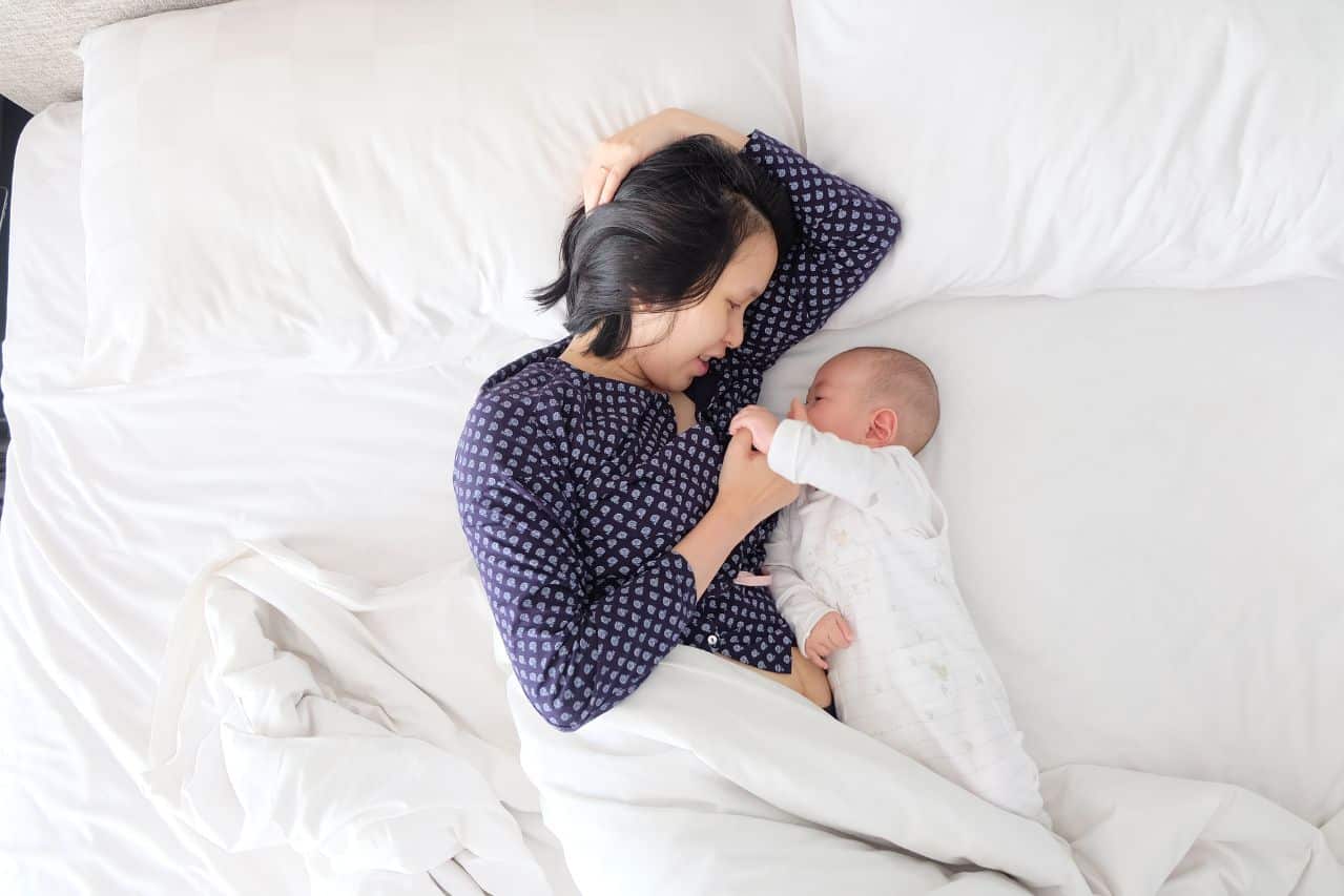 Mother lying with baby in bed.