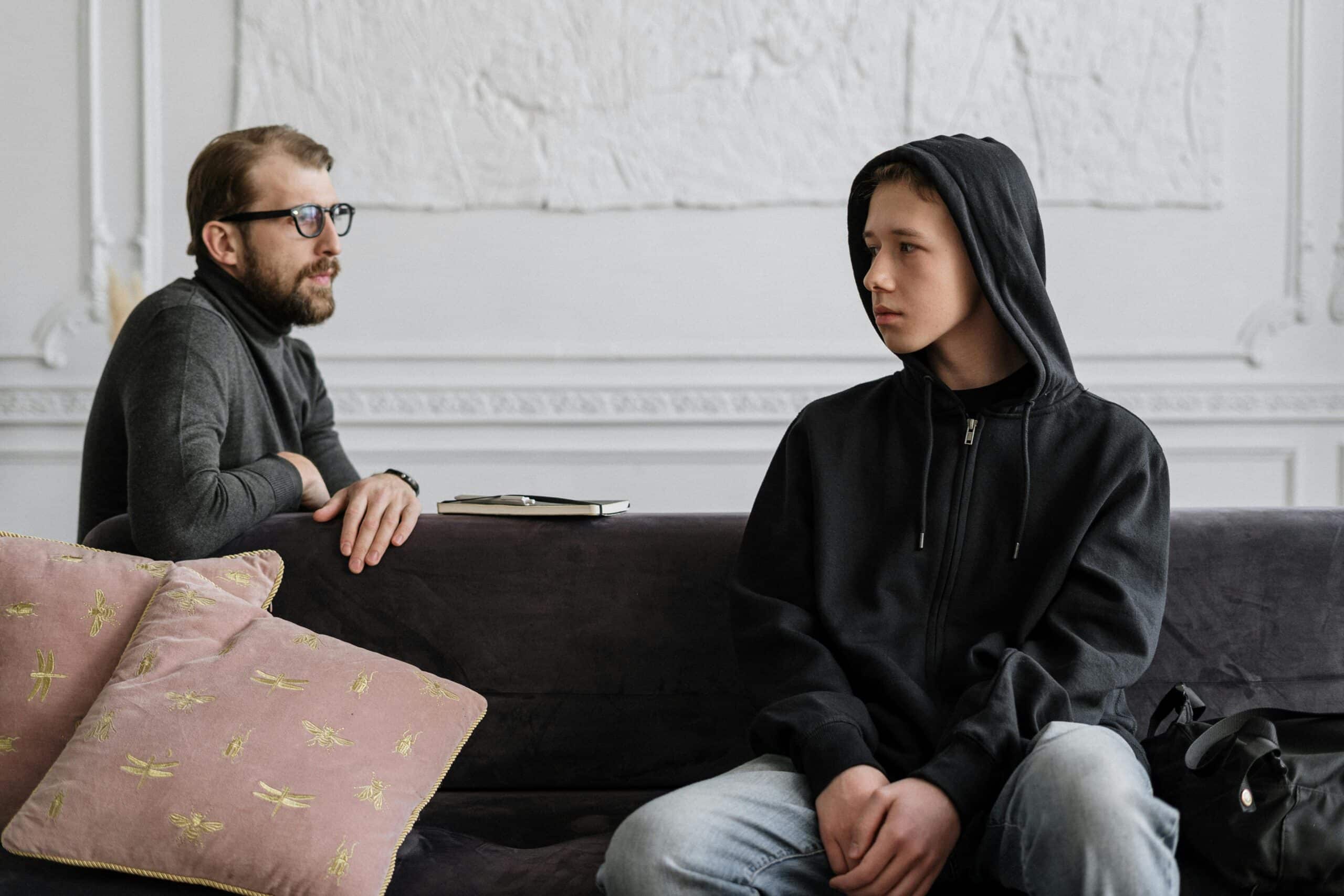 A father looks at his teenage son who looks dismissive.