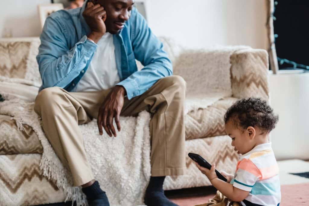 Man looking at his son playing on a phone.