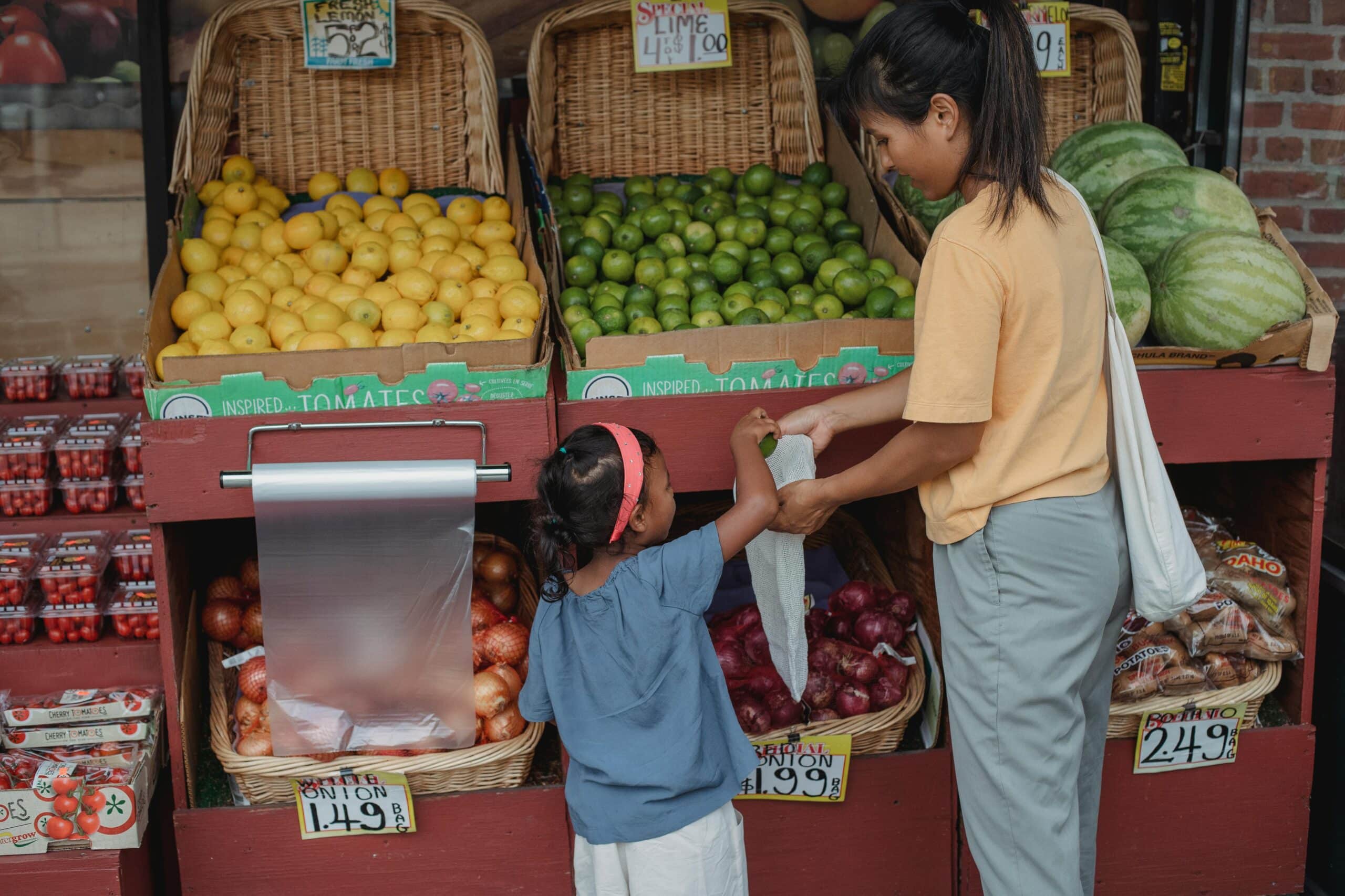 A child helping their mother select the fruit and vegetables to purchase.