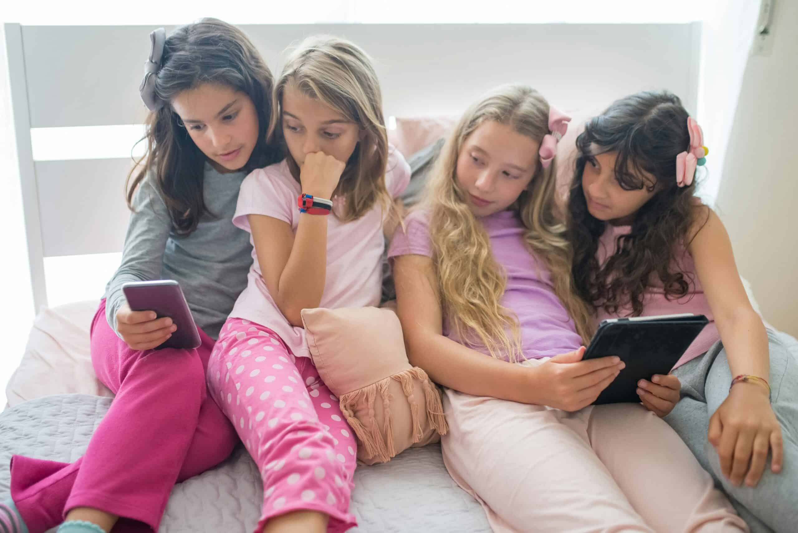 Four young girls are looking at a tablet and smartphone.