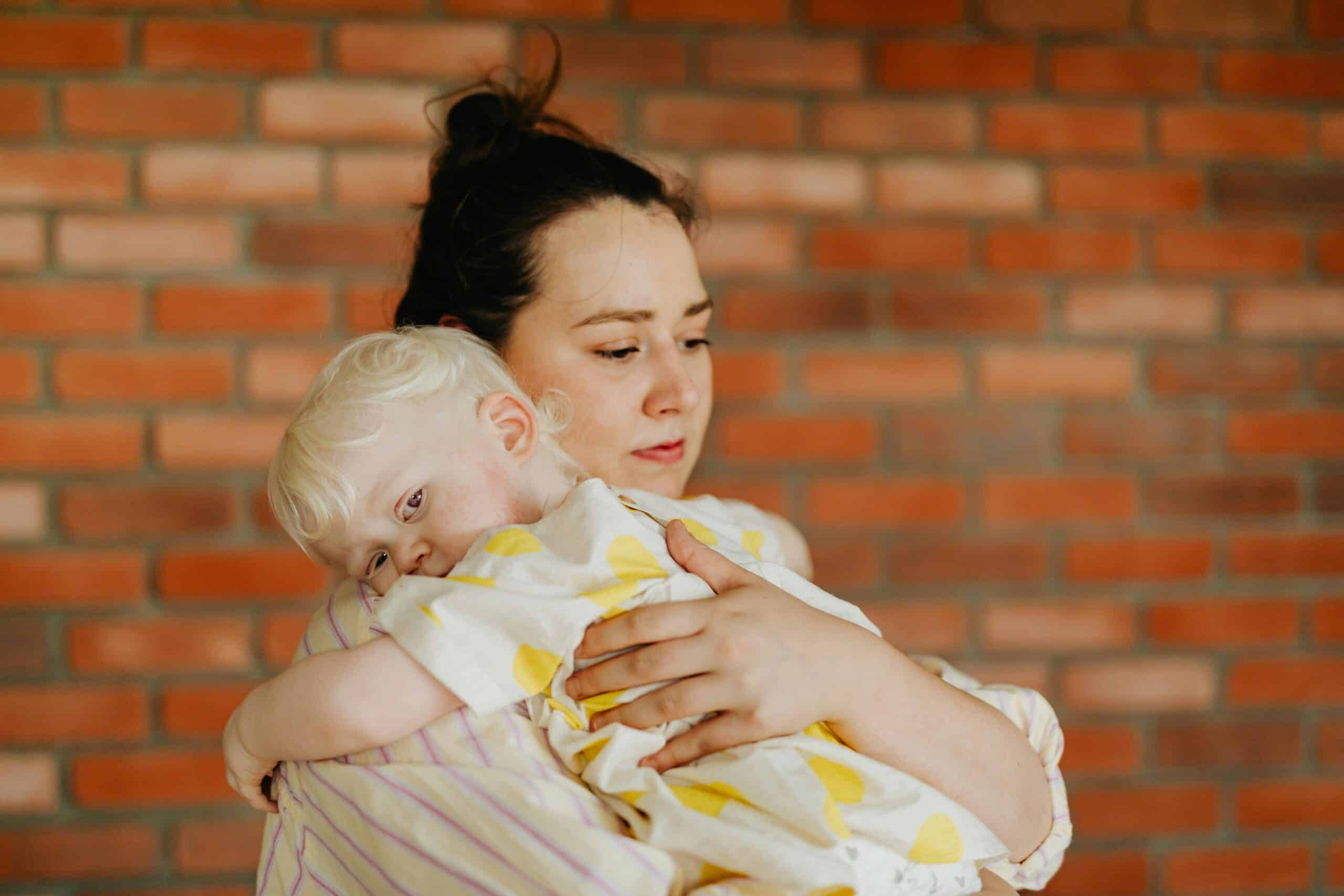 A mother hugs her young child who looks visibly sad.