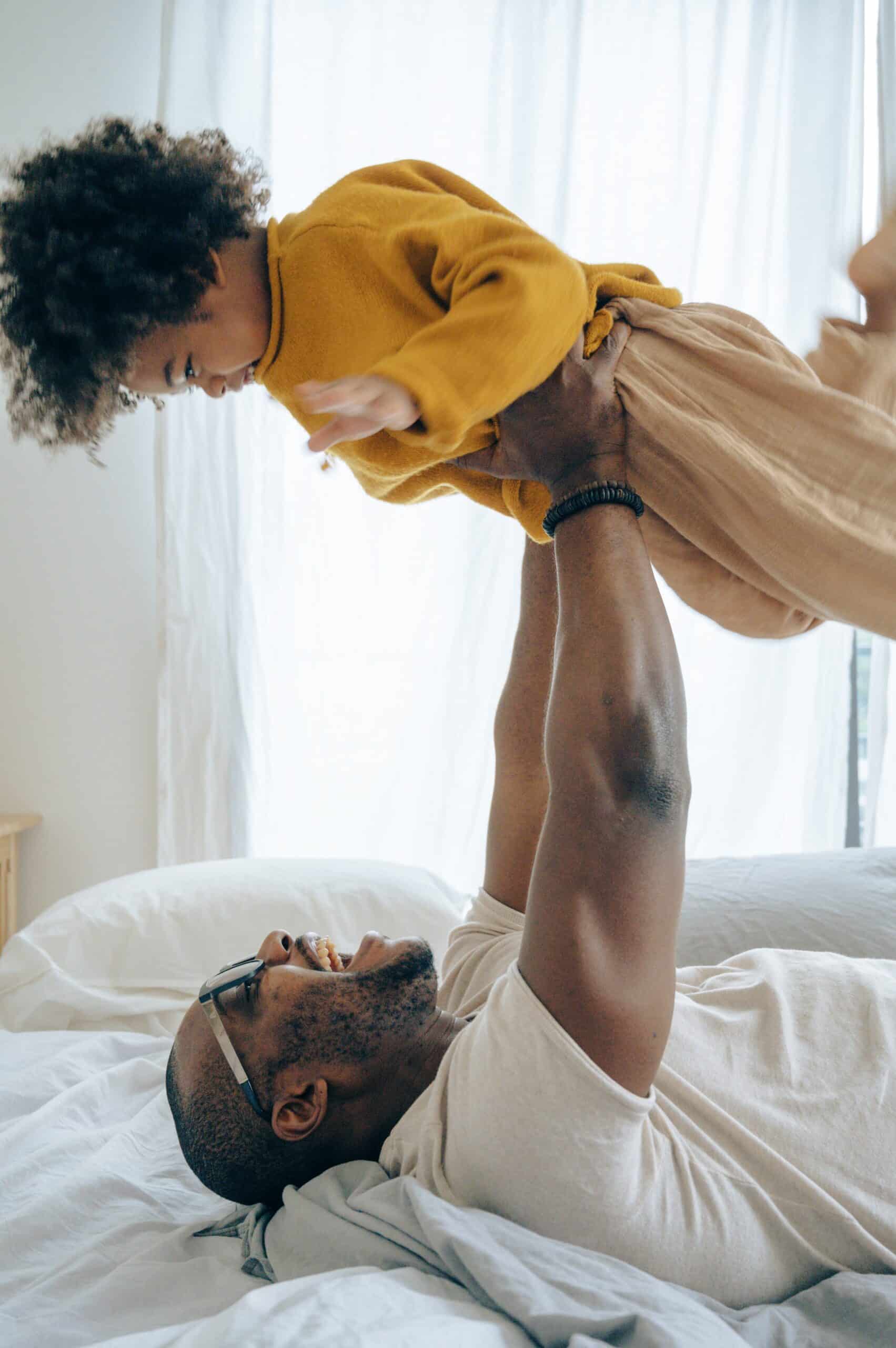 Father playing with child on bed.