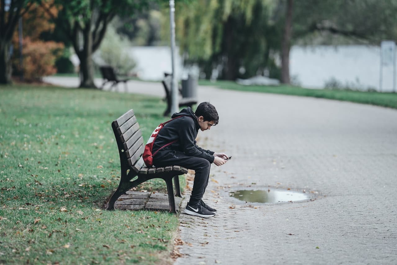 Teenage boy using mobile phone park bench.