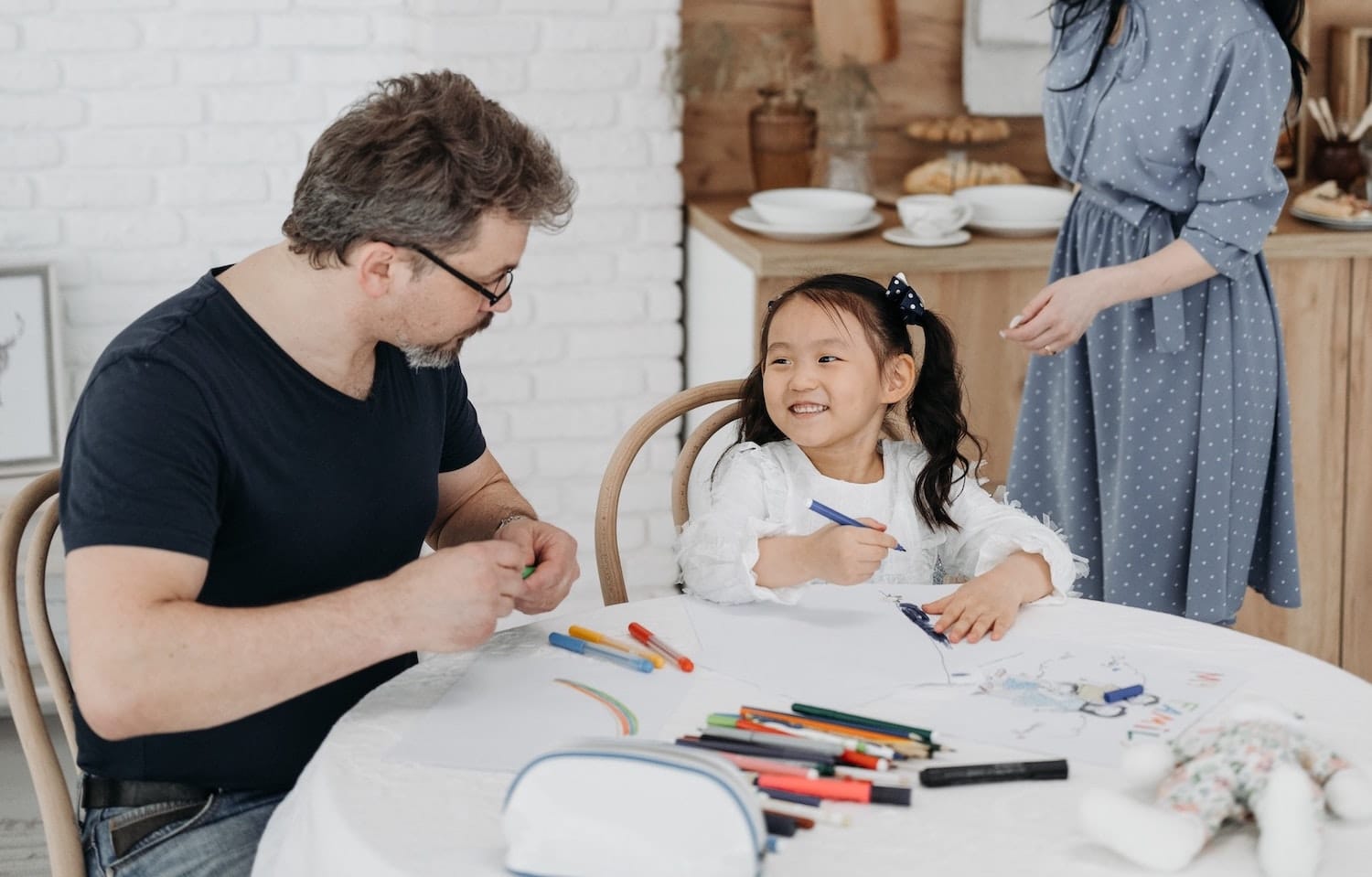 A man and a young girl playing with pens and paper on a table.