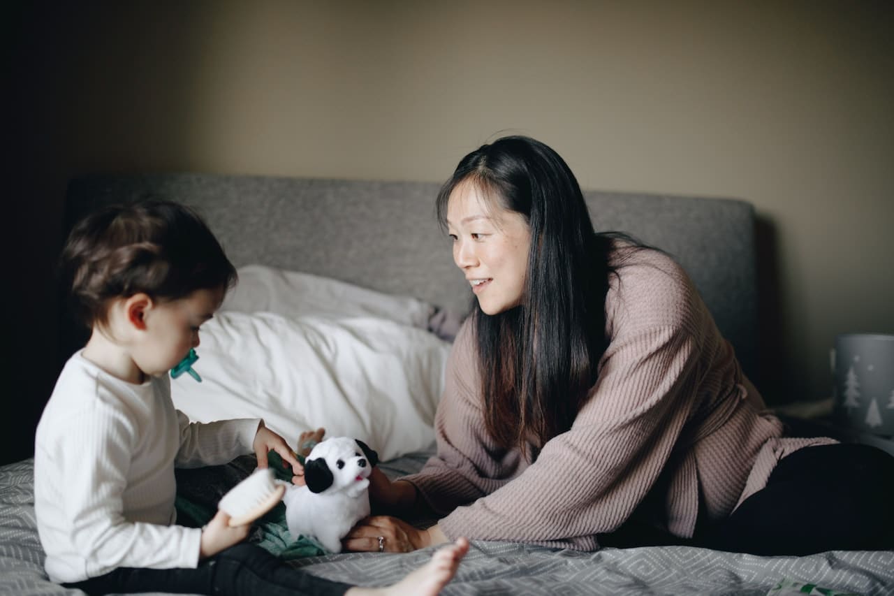 Mother and baby playing with toys on a bed.