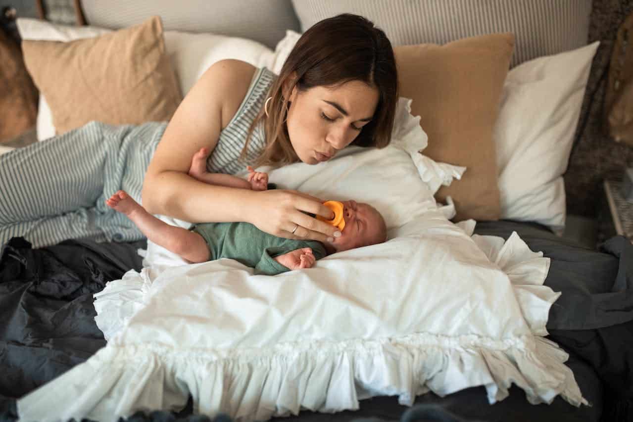 A mother putting pacifier on her crying baby's mouth.