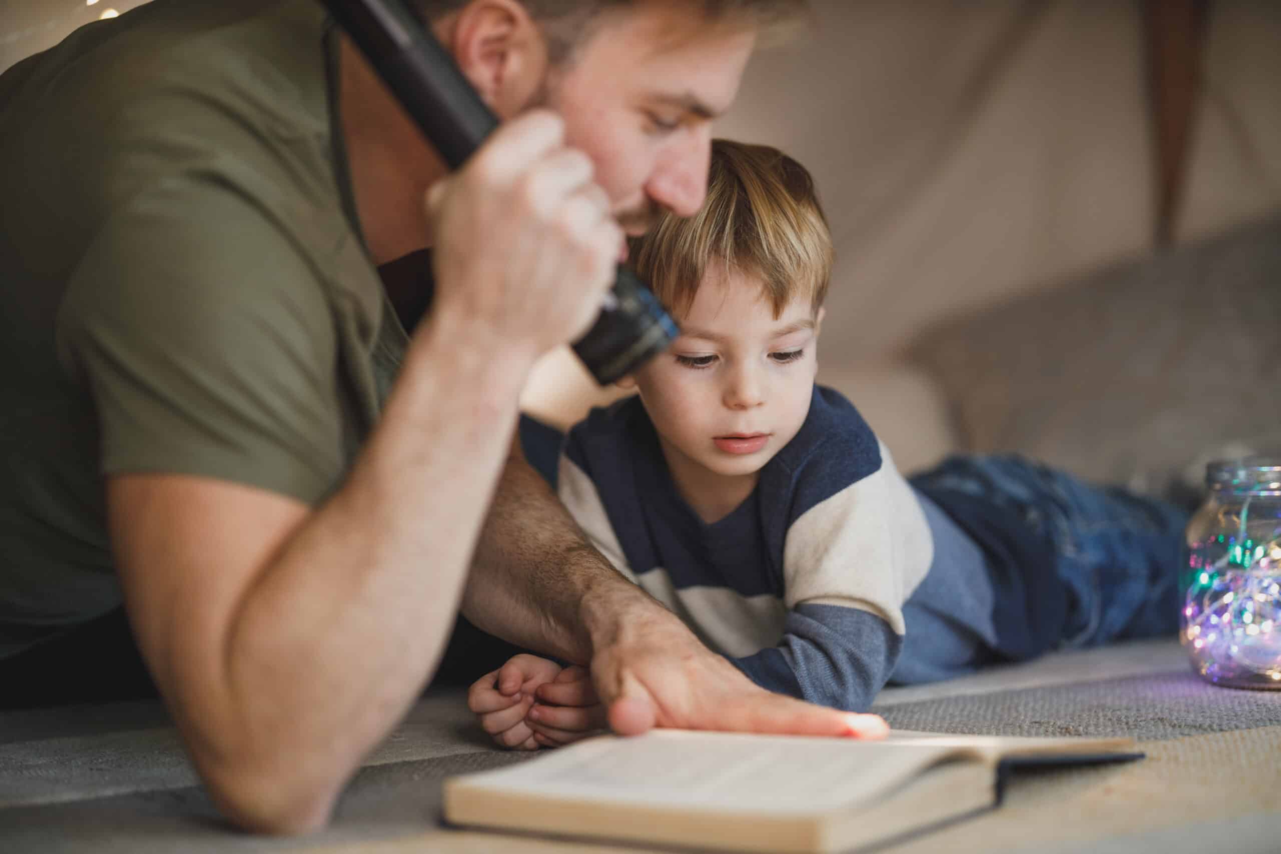 Child reading with father in a tent.